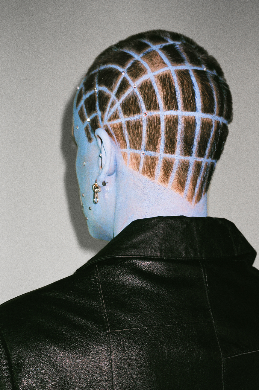 Photo of the back of a head of someone with a grid pattern shaved into their hair and blue skin